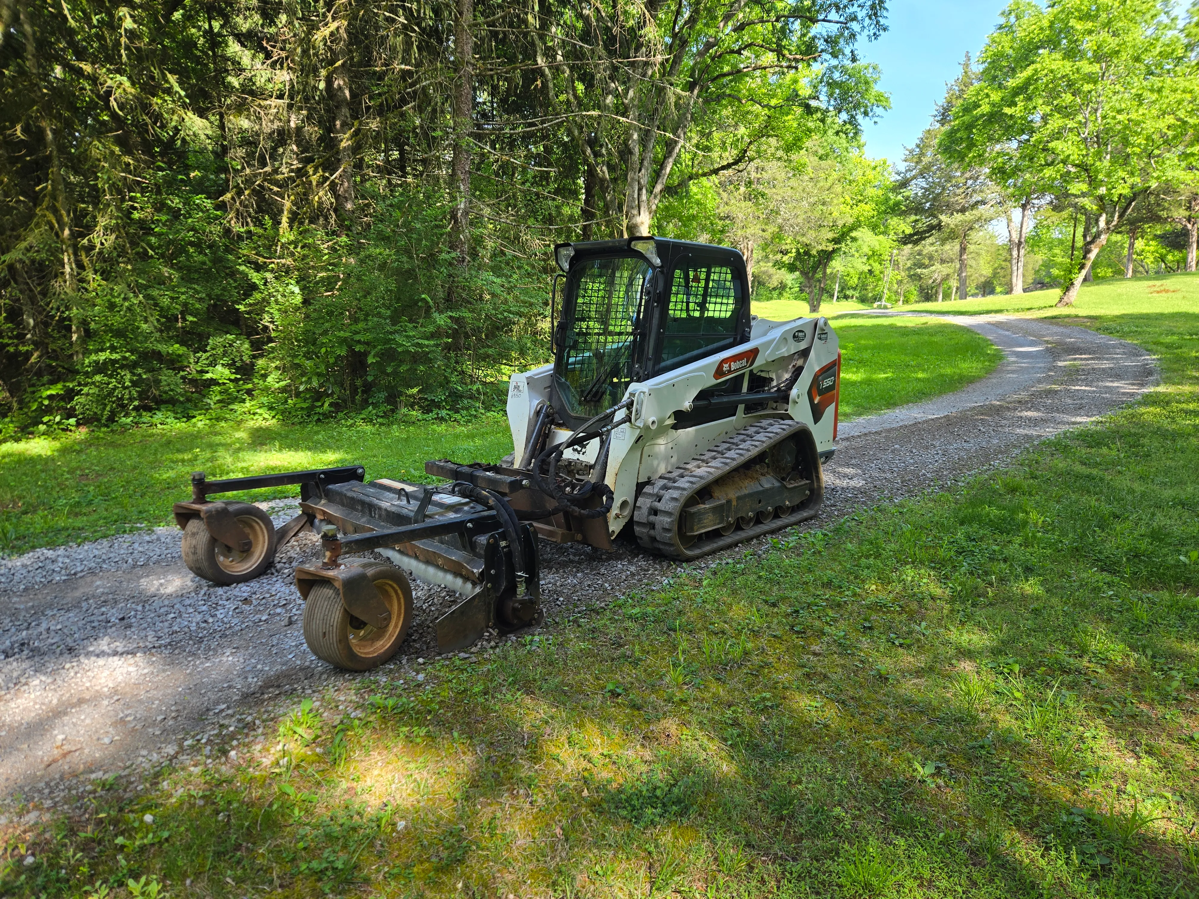 Skid steer with a power rake grading and smoothing a freshly graveled driveway in East Tennessee